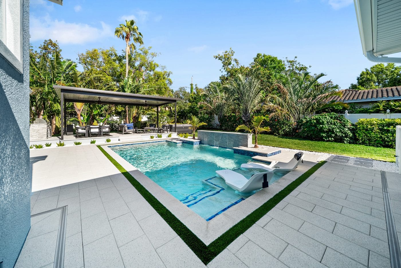 A completed Pool Perfection custom concrete pool with a raised spa, scupper water feature, in-water loungers, and travertine deck